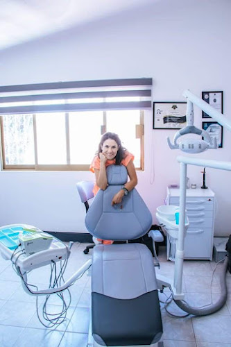 Dentista infantil en España - Una mujer con bata se apoya en un sillón dental en una moderna y luminosa consulta con equipos, una ventana y cuadros enmarcados en la pared. | Clínica dental pediátrica Dentistainfantilcercademi
