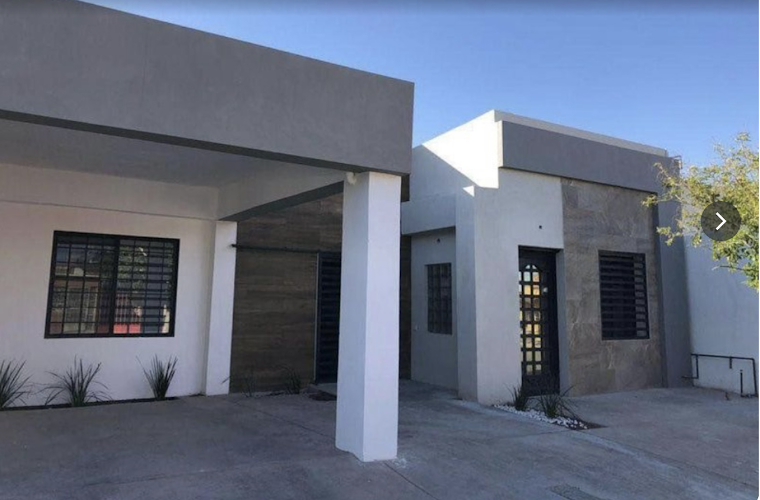 Dentista infantil en España - Moderna casa de una sola planta con tejados planos, paredes blancas y grises, grandes ventanas con rejas negras y un camino de entrada cubierto. Hay pequeñas plantas cerca de la entrada y la casa tiene un diseño minimalista. | Clínica dental pediátrica Dentistainfantilcercademi