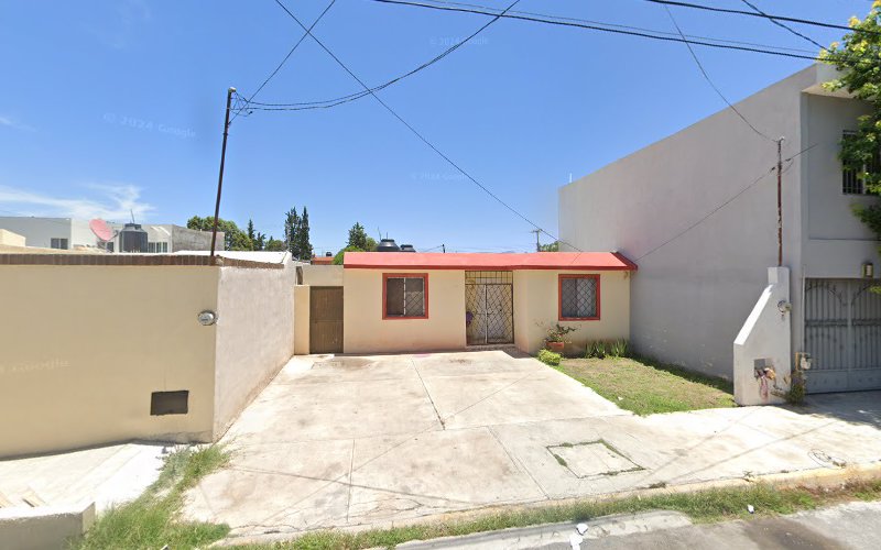 Dentista infantil en España - Casa de una sola planta con tejado rojo, paredes de color beige y ventanas enrejadas, situada entre dos edificios más altos. Delante hay una puerta con verja y un camino de entrada de hormigón. Las líneas eléctricas cruzan por encima bajo un cielo azul despejado. | Clínica dental pediátrica Dentistainfantilcercademi