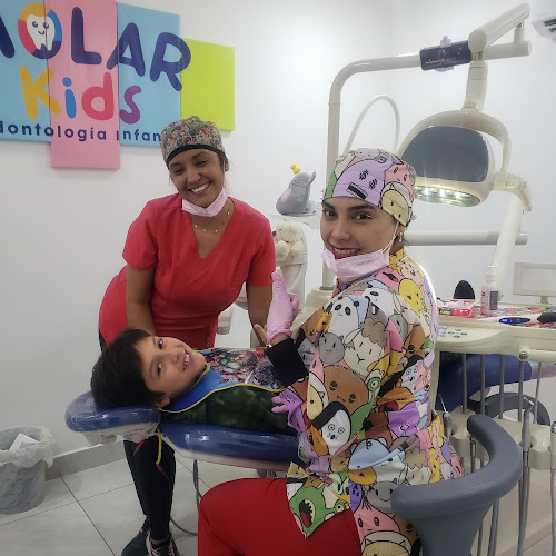 Dentista infantil en España - Dos odontólogas y un niño sonriente están sentados en una consulta dental pediátrica de colores vivos. El niño está en el sillón del dentista y el personal lleva uniformes de colores. En la pared detrás de ellas hay un cartel que dice "Molar Kids". | Clínica dental pediátrica Dentistainfantilcercademi