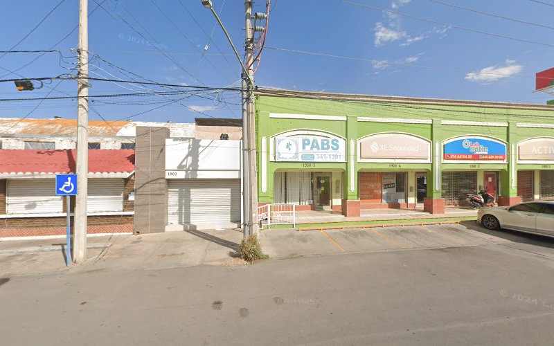 Dentista infantil en España - Vista de la calle de una hilera de edificios comerciales, incluido un edificio verde con carteles de PABS y K-Sequedad. Hay coches aparcados, un patinete, cables eléctricos y una señal azul de aparcamiento accesible delante. | Clínica dental pediátrica Dentistainfantilcercademi