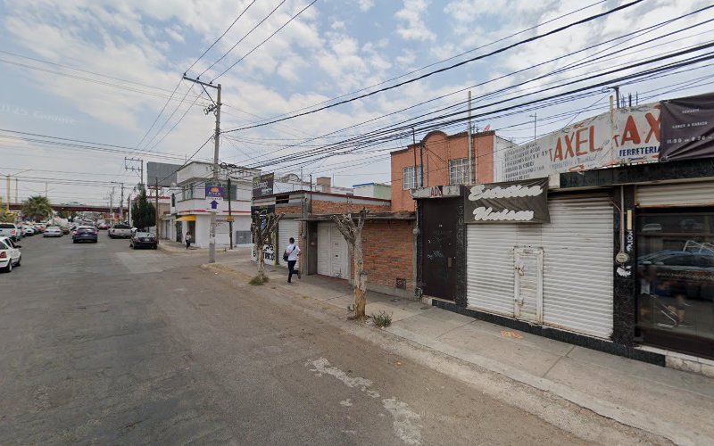 Dentista infantil en España - Una tranquila calle urbana con escaparates cerrados, unos pocos peatones, coches aparcados, líneas eléctricas aéreas y un cielo parcialmente nublado. En algunos edificios se ven carteles en español. | Clínica dental pediátrica Dentistainfantilcercademi
