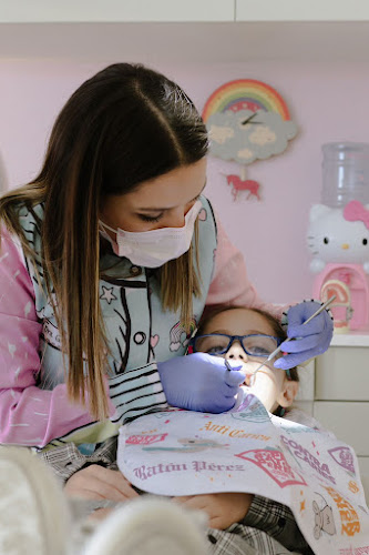 Dentista infantil en España - Una odontopediatra en León con mascarilla y guantes examina los dientes de un niño en una clínica dental decorada con colores pastel y personajes de dibujos animados. El niño, con gafas y babero, se sienta tranquilamente en el alegre entorno. | Clínica dental pediátrica Dentistainfantilcercademi