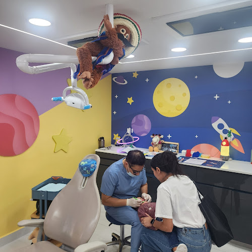 Dentista infantil en España - Un dentista examina a un niño en una colorida clínica de temática espacial. Planetas y cohetes decoran la pared. Una mujer está de pie junto al niño. Un perezoso de peluche con sombrero cuelga de la lámpara dental sobre el sillón. | Clínica dental pediátrica Dentistainfantilcercademi