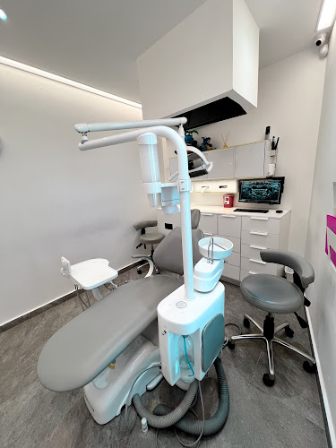 Dentista infantil en España - Un consultorio dental moderno con un sillón dental gris, luz cenital, instrumentos dentales, armarios blancos, un monitor de ordenador y un taburete gris sobre un suelo de baldosas grises. La sala está limpia y bien iluminada. | Clínica dental pediátrica Dentistainfantilcercademi