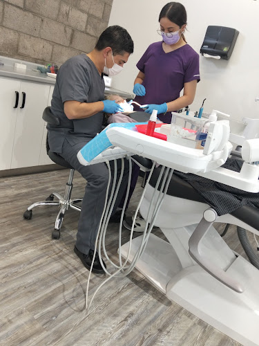 Dentista infantil en España - Un dentista y un auxiliar de odontología con mascarilla y guantes atienden a un paciente en una moderna consulta dental en la que se ven diversos instrumentos y equipos odontológicos. | Clínica dental pediátrica Dentistainfantilcercademi