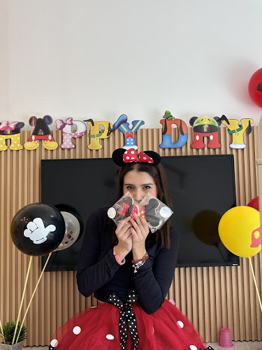 Dentista infantil en España - Una mujer vestida con un disfraz de Minnie Mouse está de pie delante de un cartel de "FELIZ DÍA", sosteniendo tazas temáticas delante de su cara. Está rodeada de globos y adornos de Mickey y Minnie Mouse. | Clínica dental pediátrica Dentistainfantilcercademi