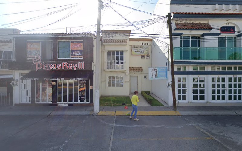 Dentista infantil en España - Una persona con camisa amarilla camina por una banqueta frente a Pizzas Rey III, con edificios residenciales y comerciales cerca, incluyendo una odontopediatra en Irapuato, todo bajo un cielo despejado. | Clínica dental pediátrica Dentistainfantilcercademi