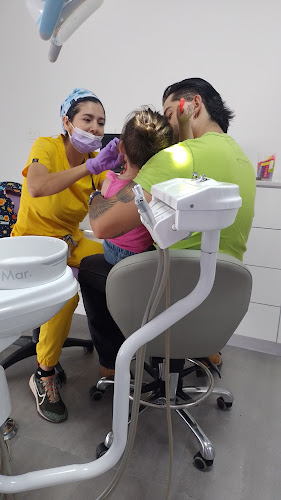 Dentista infantil en España - Un dentista con bata amarilla examina la boca de un niño pequeño sentado en el regazo de un adulto en una clínica dental. El adulto consuela al niño durante la revisión dental. | Clínica dental pediátrica Dentistainfantilcercademi