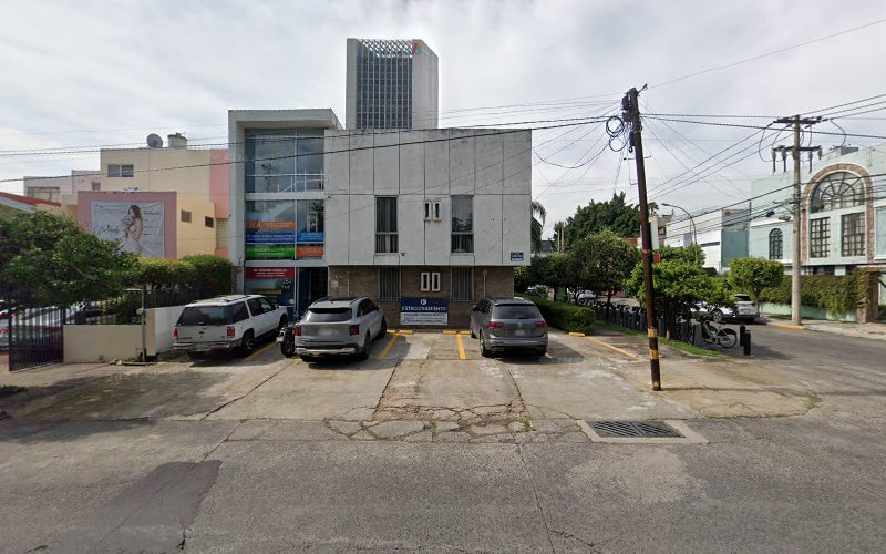 Dentista infantil en España - Un moderno edificio de oficinas de dos plantas con fachada de cristal y piedra tiene tres todoterrenos aparcados delante y está rodeado de otros edificios, árboles, tendidos eléctricos y un cielo nublado. | Clínica dental pediátrica Dentistainfantilcercademi