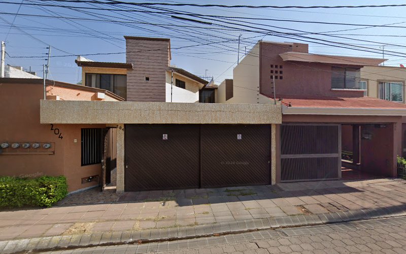 Dentista infantil en España - Dos casas modernas contiguas con grandes puertas de garaje marrones, tejados planos y fachadas de color beige y rojo. La acera tiene pequeñas plantas y se ven varios contadores de electricidad en el lado izquierdo. Los cables aéreos de los servicios públicos cruzan la escena. | Clínica dental pediátrica Dentistainfantilcercademi